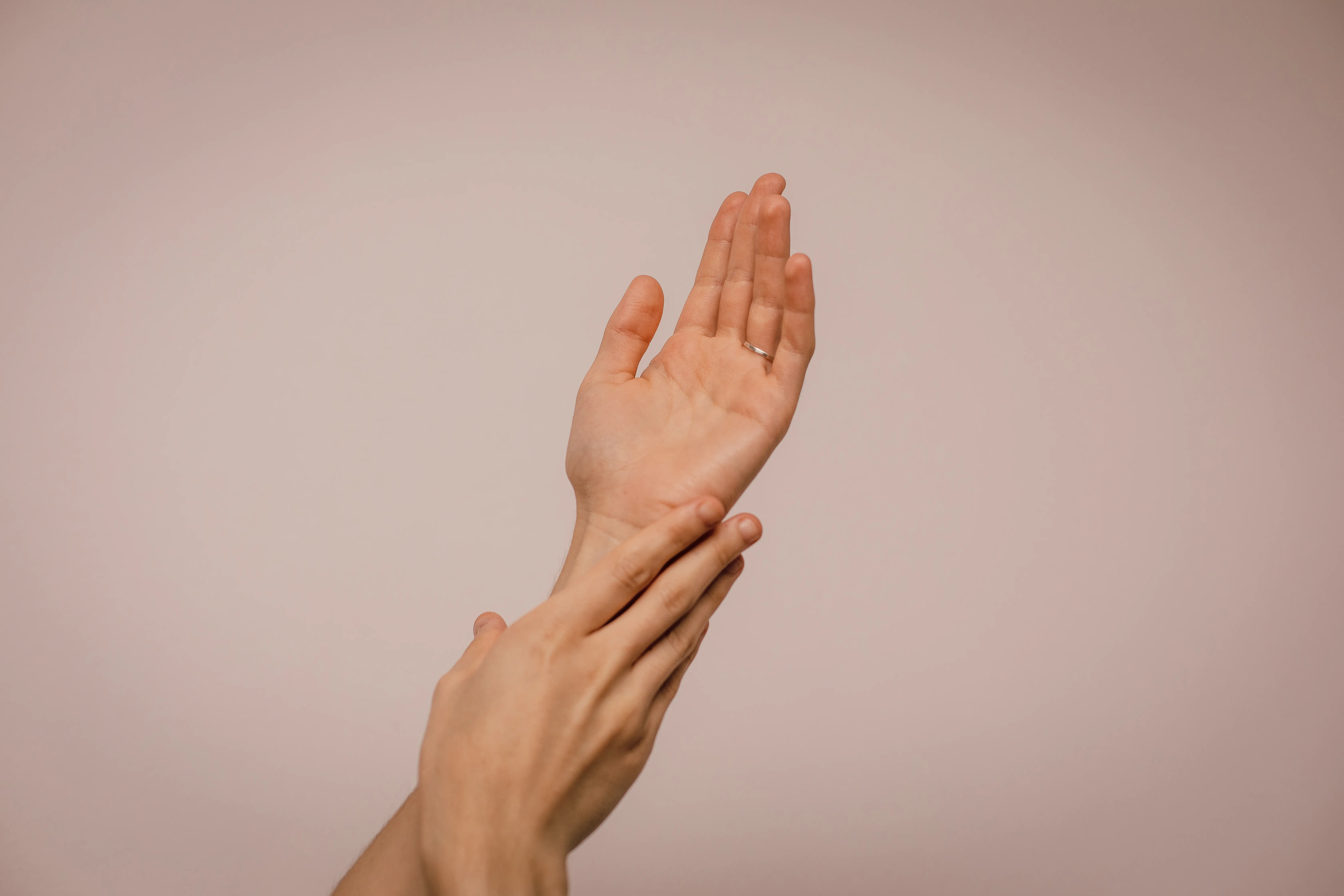 Close-up of two hands reaching toward each other against a plain pink background, soft and calm mood