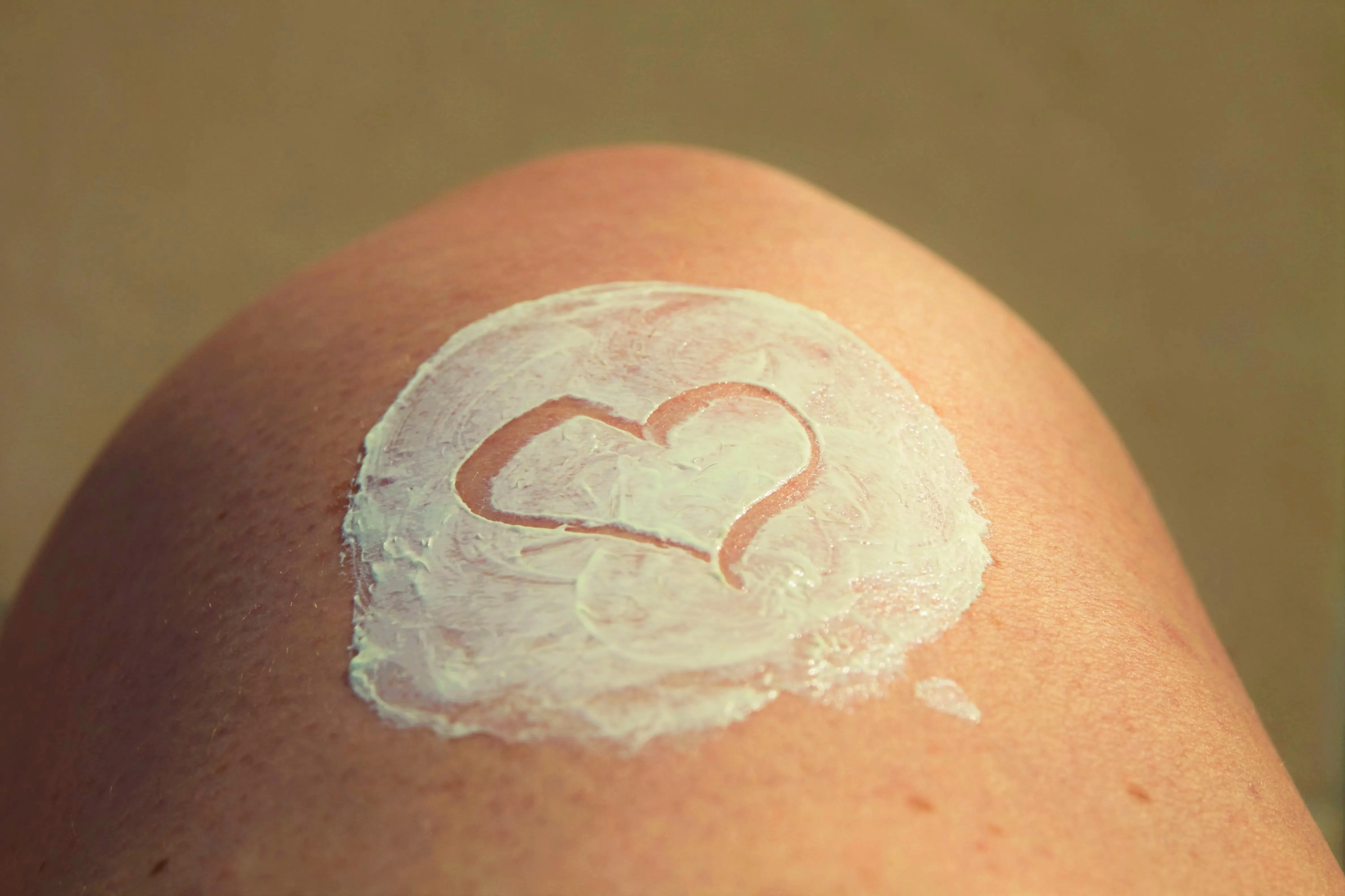 Close-up of a knee with sunscreen or lotion spread in a circle with a heart drawn in it, warm skin tones