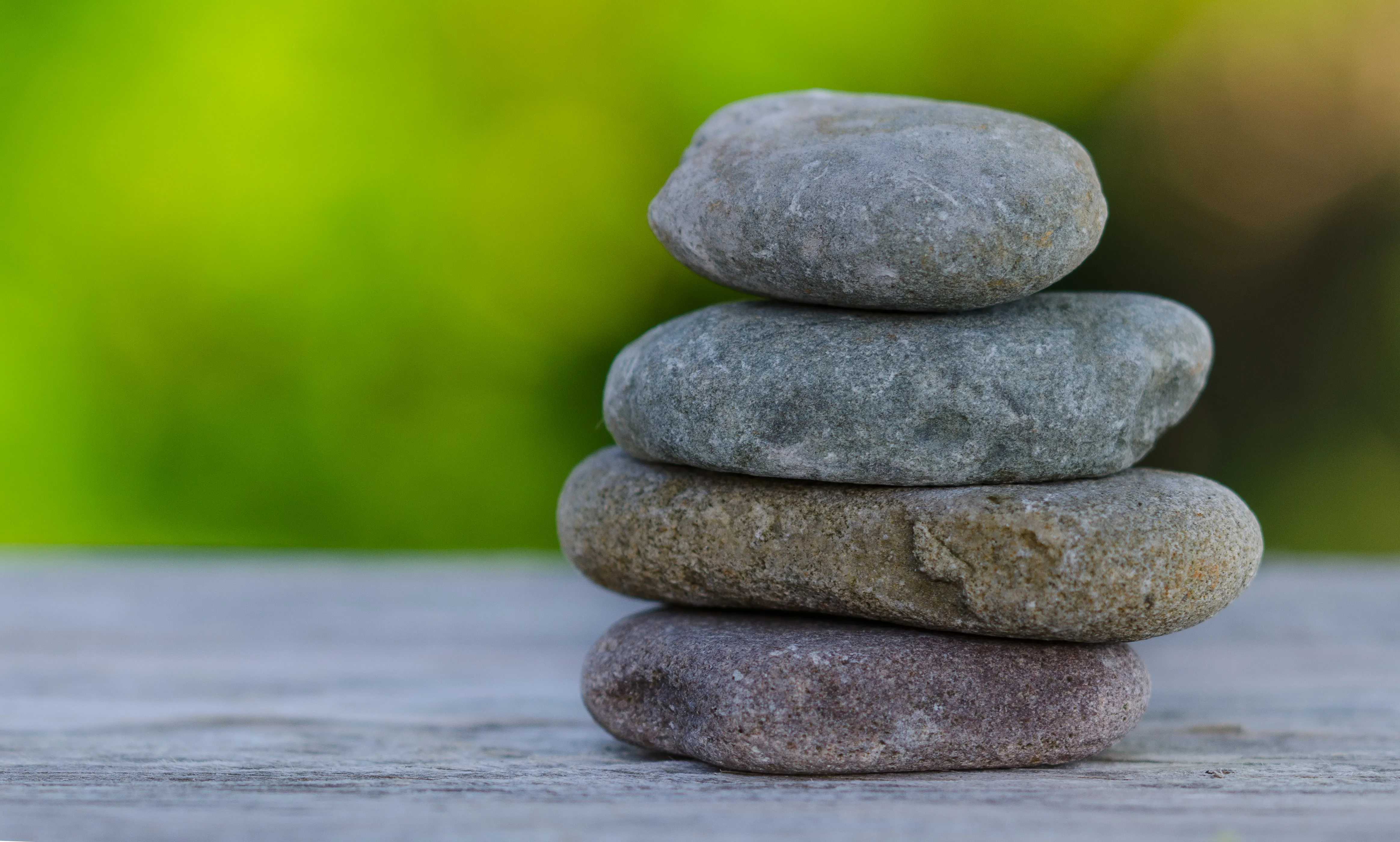 Stack of four smooth balanced stones on a wooden surface with a blurred green background, calm zen mood